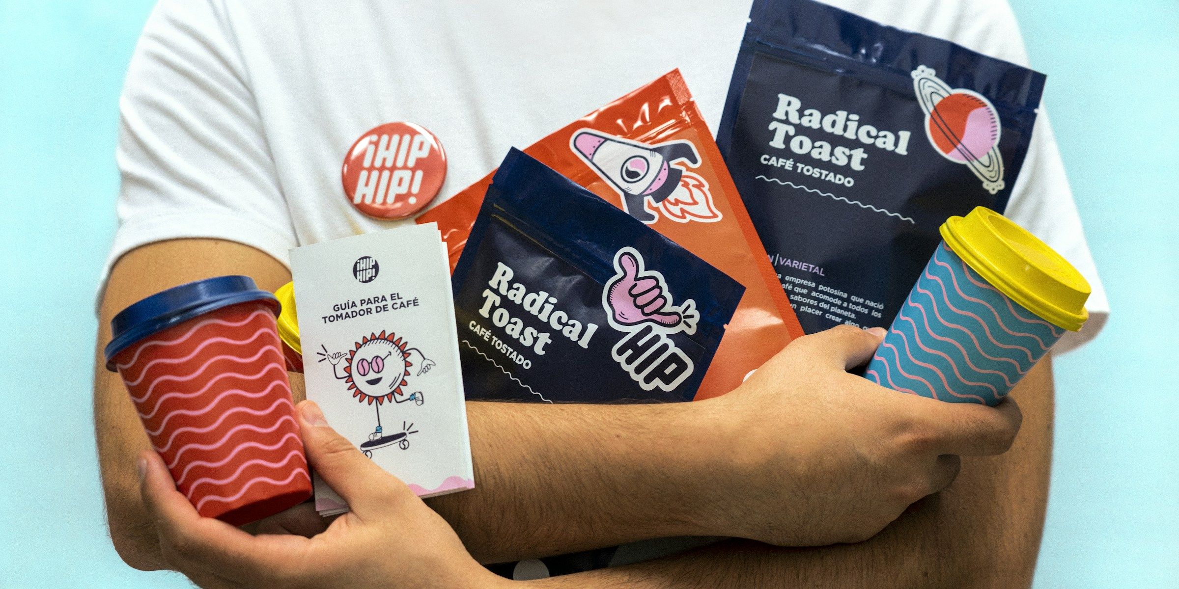 Coffee packaging, cups and merch held against a white tee